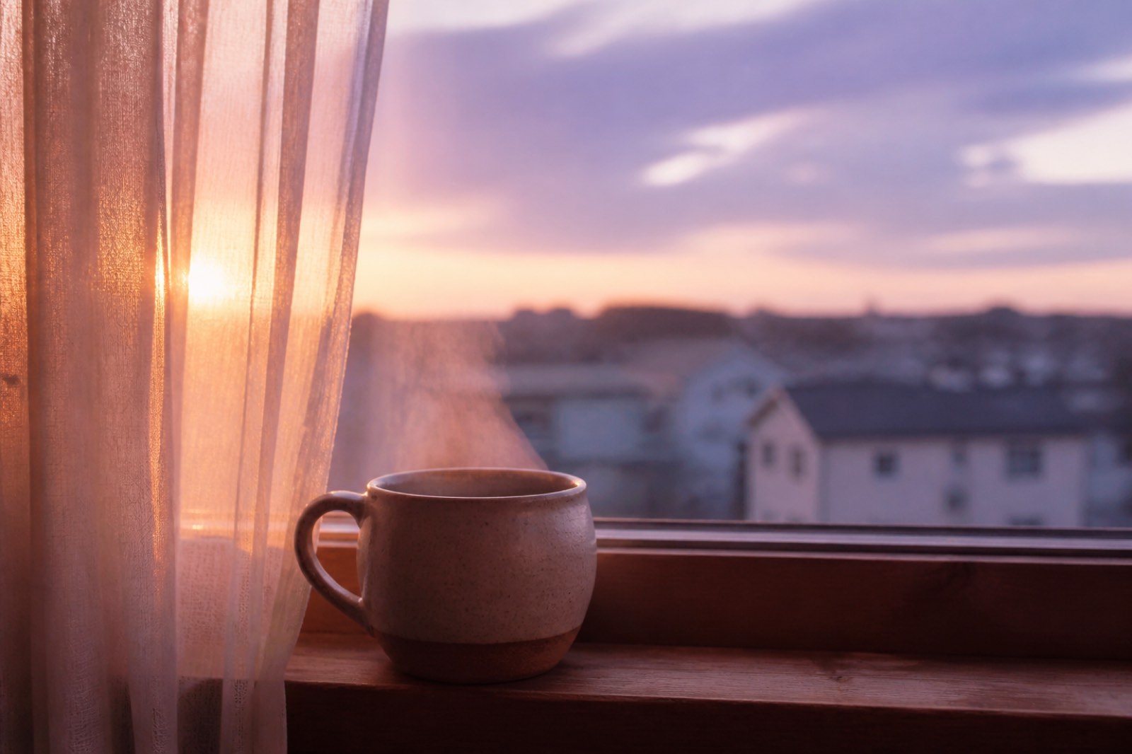 A ceramic mug of steaming tea on a wooden windowsill at dawn, purple morning sky beyond